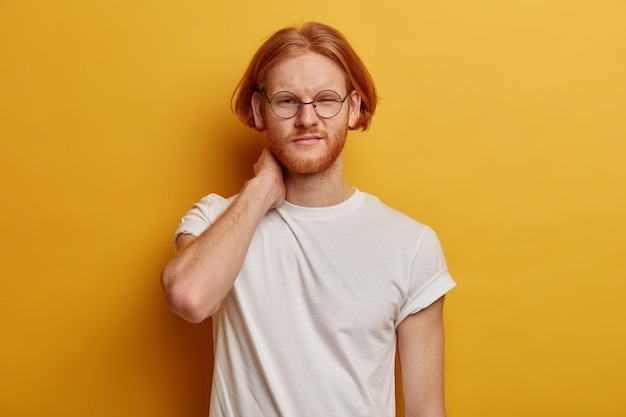 Serious displeased man with bob hairstyle, ginger beard, touches necK