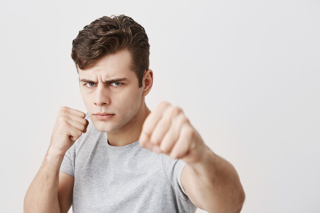 Serious displeased muscular young caucasian male frowns face in displeasure, shows clenched fists, demonstrates strength and irritation, annoyed with someone. Negative emotions concept.