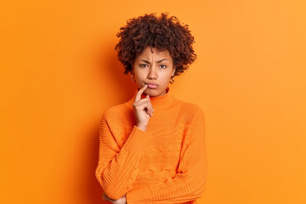 Serious displeased young African American woman frowns face keeps finger near lips