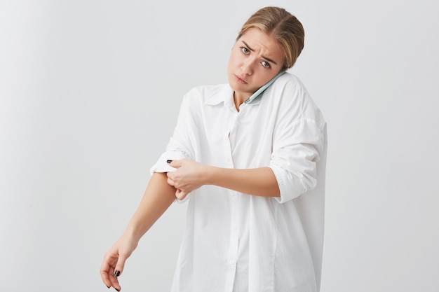 Serious dissatisfied young female entrepreneur talking on mobile phone with business partner rolling sleeve of her white shirt Blonde girl having phone conversation