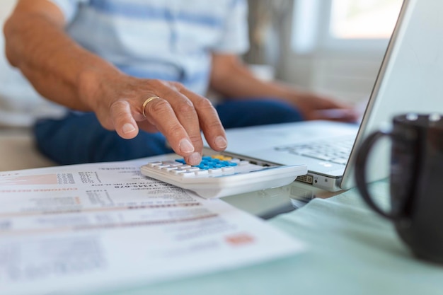 Serious elder senior greyhaired grandpa using calculator counting bank loan payment holding papers at home focused mature old man doing paperwork calculating bills managing finances sit on sofa