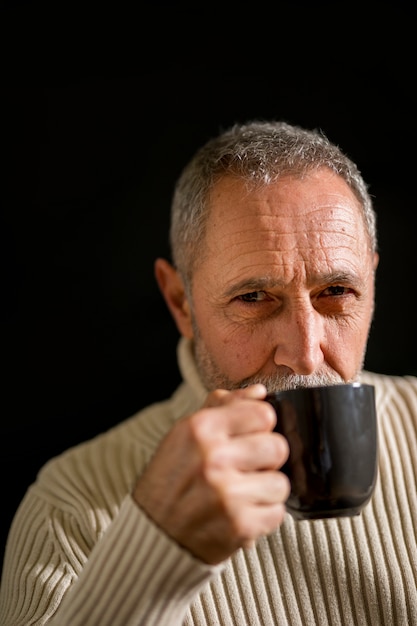 Serious elderly male drinking and looking at camera