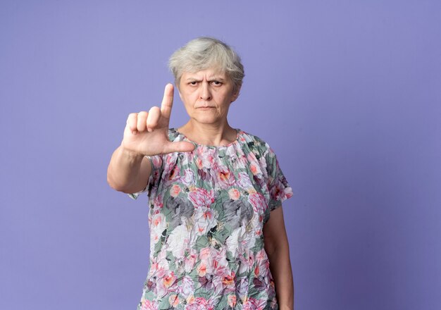 Serious elderly woman points up isolated on purple wall