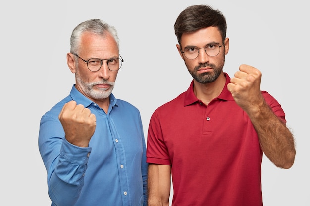 Free photo serious father and young adult son posing against the white wall