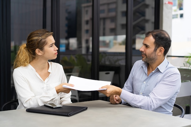 Serious female client giving document to financial consultant