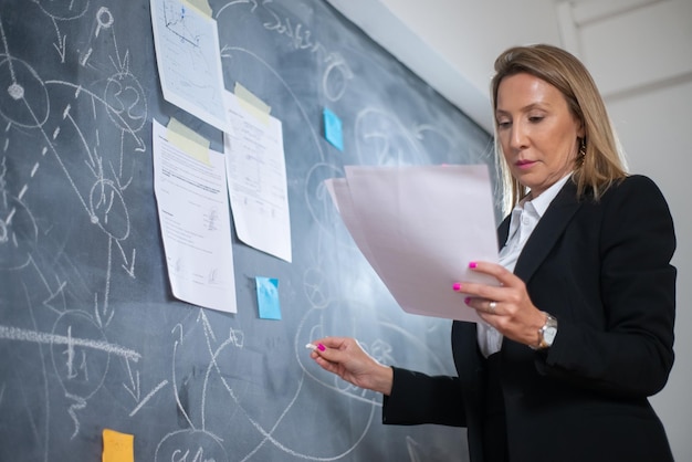 Free photo serious female financier analyzing business growth. low angle view of woman analyzing financial data, drawing graphs of profit growth with chalk on board. financial analysis, business growth concept