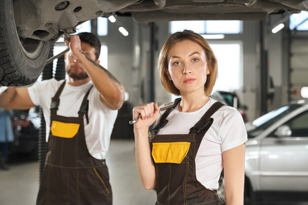 Serious female mechanic looking at camera and keeping wrench