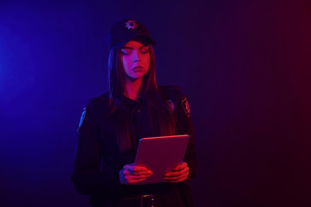Serious female police officer is posing for the camera against a black background with red and blue ...