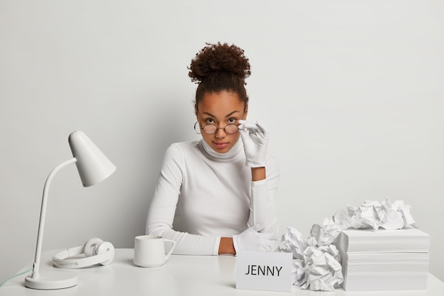 Free photo serious female secretary looks attentively through glasses, wears white gloves