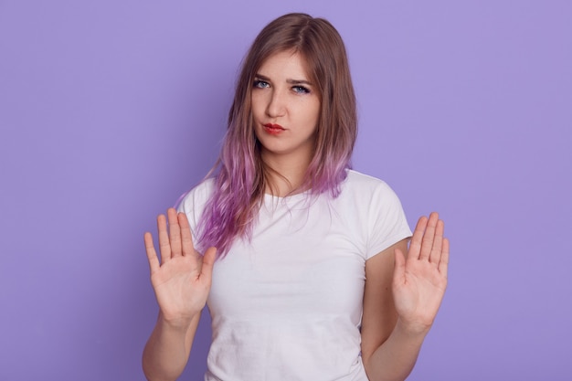 Serious female showing palms to camera, looking with strict expressing and ban gesture, forbids somebody to do bad things, isolated over purple wall.