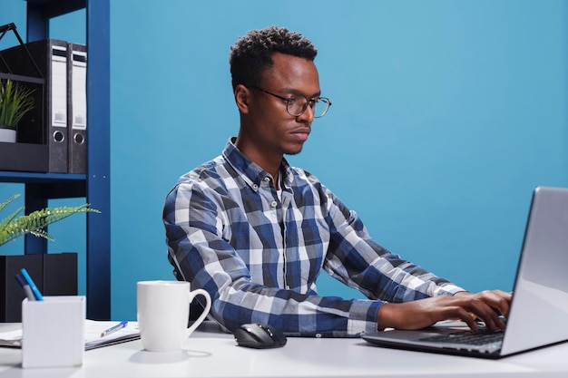 Serious firm project manager sitting at desk in modern office while using laptop to develop marketing strategy. Confident company employee using work computer to analyze accounting documentation.