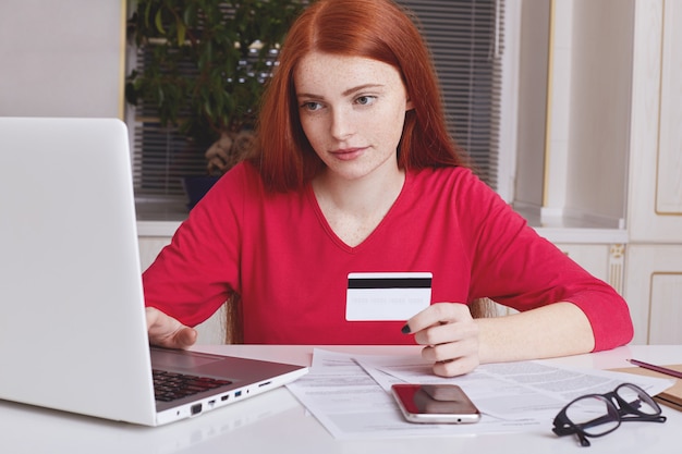 Serious freckled ginger female uses laptop computer for e commerce