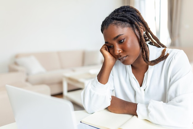 심각한 얼굴을 찡그린 아프리카계 미국인 여성은 직장 책상에 앉아 노트북 화면을 보고 이메일을 읽고 걱정스러워 합니다. 지루하고 피곤한 직원 문제 앱 문제