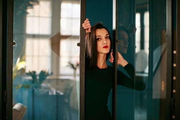 A serious girl stands near a glass door