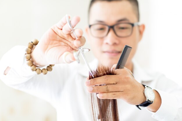 Serious hairdresser cutting hair with scissors