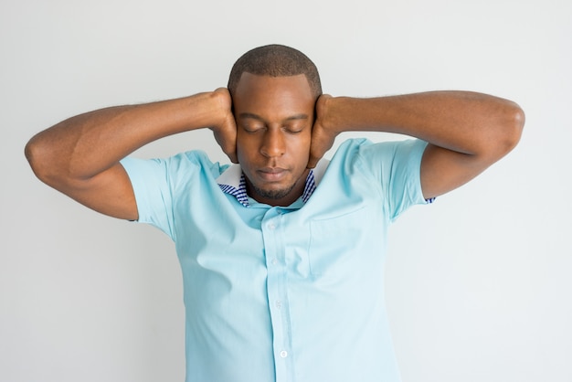 青いTシャツの真面目なハンサムなアフリカ男は、耳を覆っている間に思考に集中しています