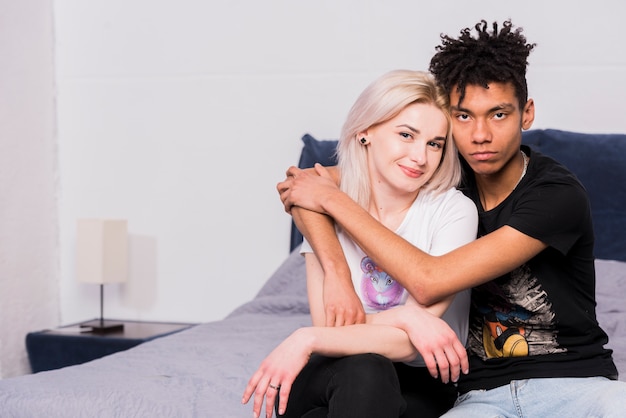 Adolescente africano bello serio che abbraccia la sua amica che si siede sul letto