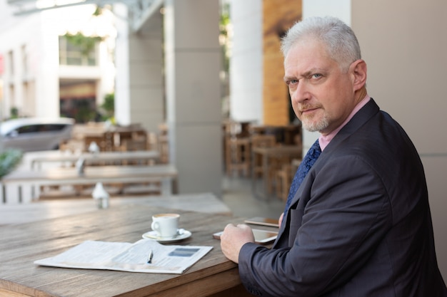 Serious handsome businessman in suit working in sidewalk cafe