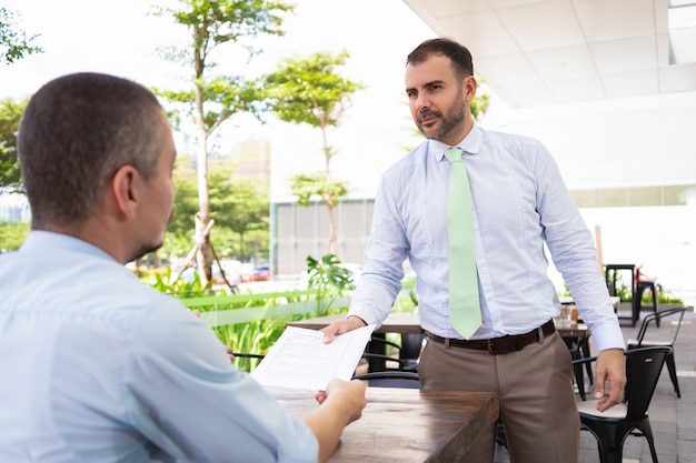 Serious handsome Hispanic man bringing papers to manager