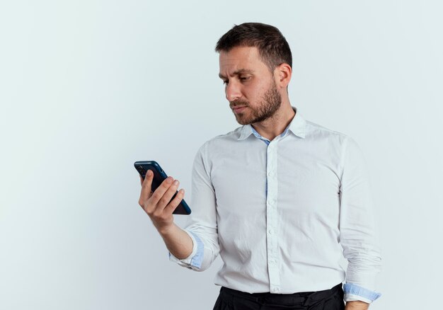 Serious handsome man holds and looks at phone isolated on white wall