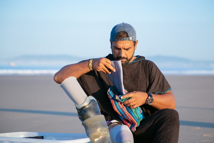 Free Photo serious handsome young man sitting on beach and putting on below-knee prosthesis