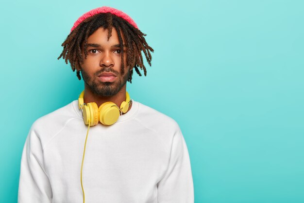향취를 가진 심각한 힙 스터 남자는 분홍색 모자와 흰색 스웨터를 입고 오디오 트랙을 듣기위한 헤드폰을 가지고 있으며 항상 음악을 듣는 자유 시간을 보냅니다.