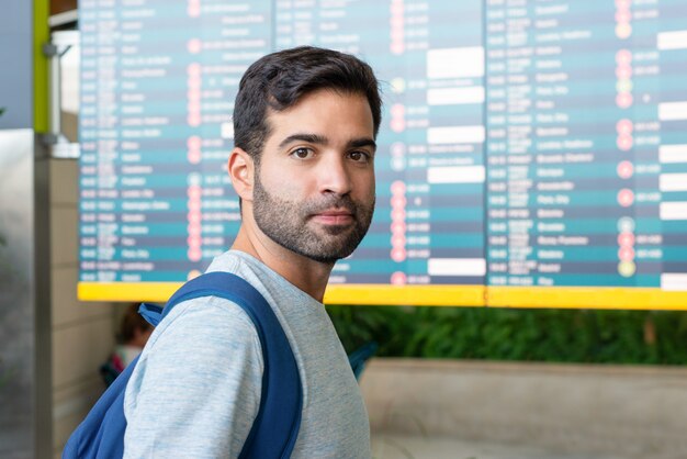 Serious Hispanic man posing near departure board