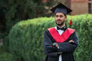 Бесплатное фото Серьезный индийский выпускник в выпускном халате со скрещенными руками смотрит вперед