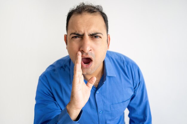 Serious Indian man holding hand near mouth and shouting loud