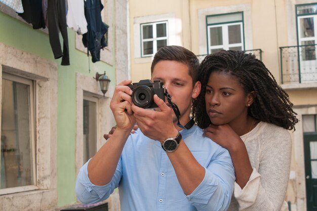 Serious interracial couple taking photos on camera in city