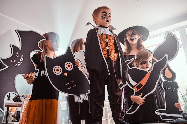 Serious kids in Halloween costumes are posing for photographer while holding decorations.