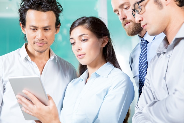 Serious Lady Showing Tablet Screen to Colleagues