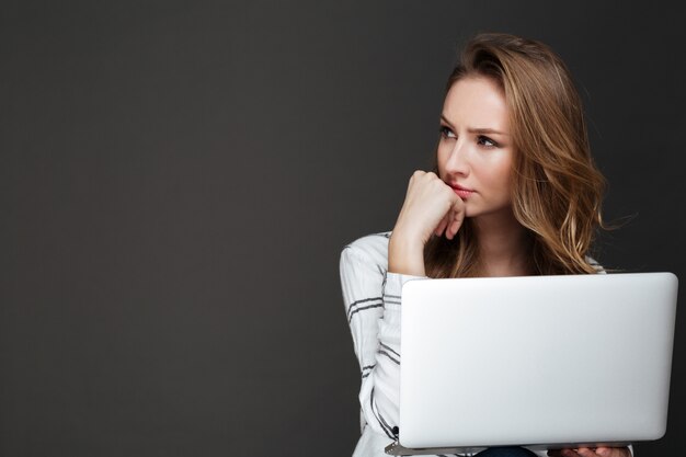 Serious lady using laptop over dark wall