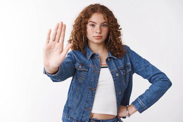 Serious-looking assertive curly-haired young girl show palm stop gesture