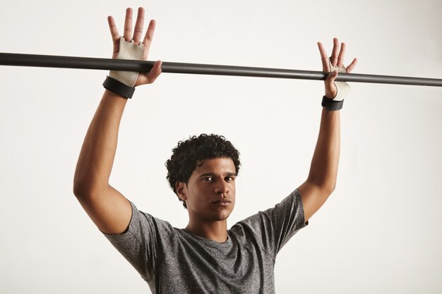 serious looking black gymnast in gray tshirt and gymnastics hand protection preparing to grab a black carbon pullup bar, fingers outstretched, isolated on white
