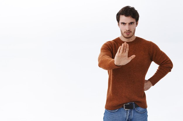 Serious-looking and confident young strong handsome man in casual outfit pull hand forward to show stop gesture