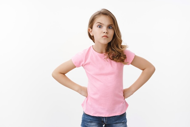 Free photo serious-looking strict and angry little arrogant girl, blond child, stand in bossy offended pose, hold hands waist demand answers