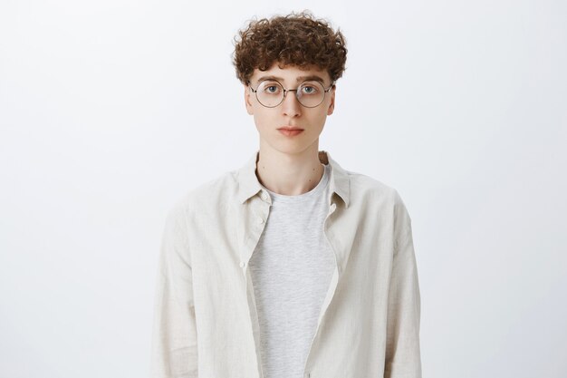 Serious-looking teenage guy posing against the white wall