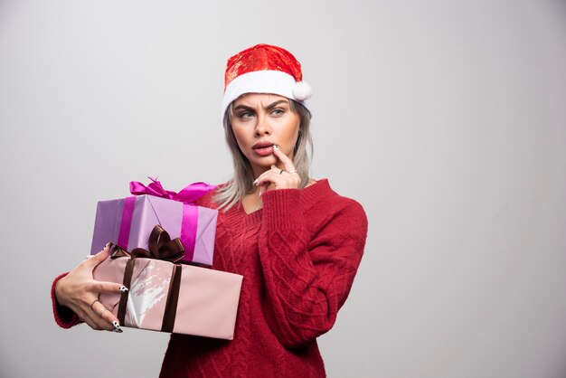 Serious looking woman in Santa hat holding Christmas gifts.