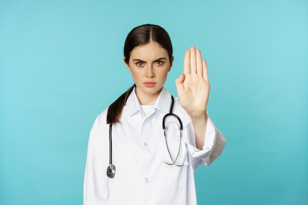 Serious looking young doctor woman medical clinic worker showing stop prohibition forbidding gesture...