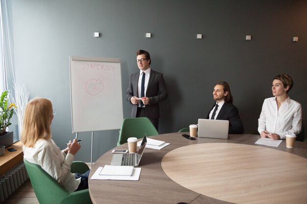 Serious male coach giving presentation on flipchart to business colleagues