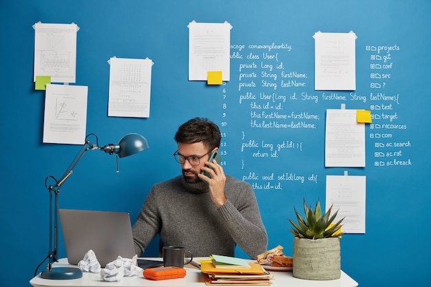 Free photo serious male designer focused in screen of laptop computer, concentrated on analyzing information, thinks about report during distance job