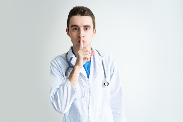 Serious male doctor showing silence gesture