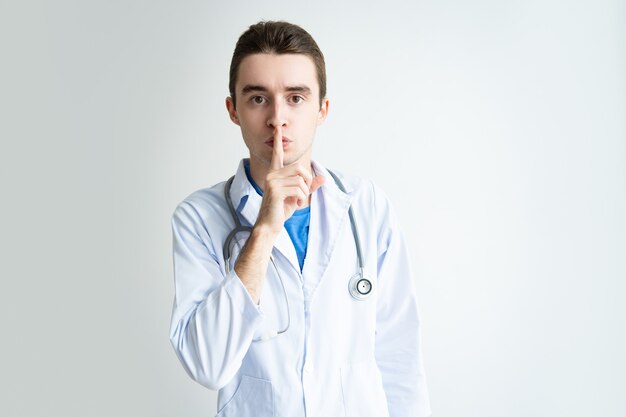Serious male doctor showing silence gesture