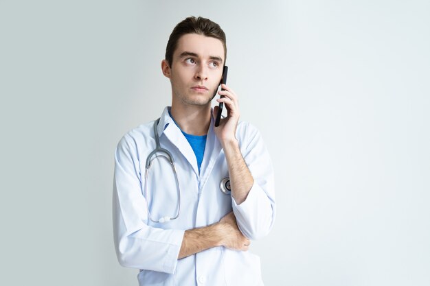 Serious male doctor talking on smartphone