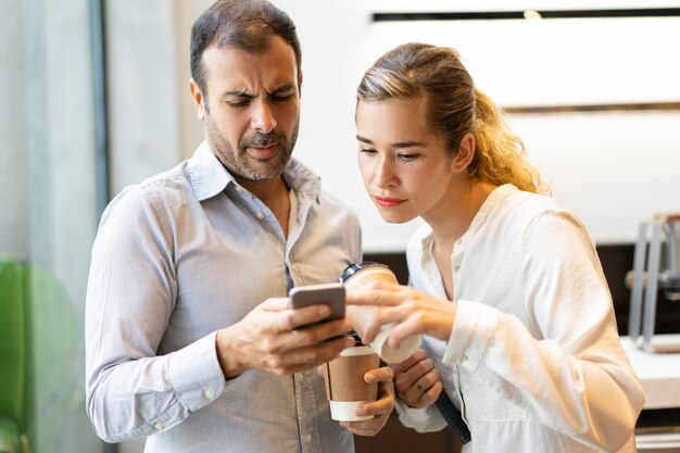 Serious male and female colleagues reading message on cellphone