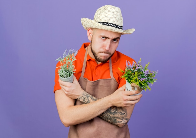 Serious male gardener wearing gardening hat holds flowerpots