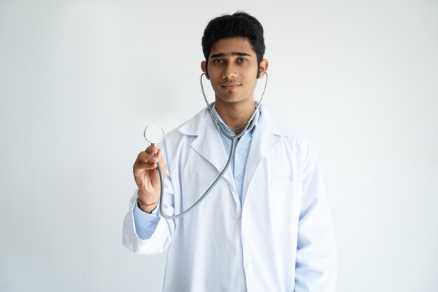 Serious male general practitioner using stethoscope and looking at camera.