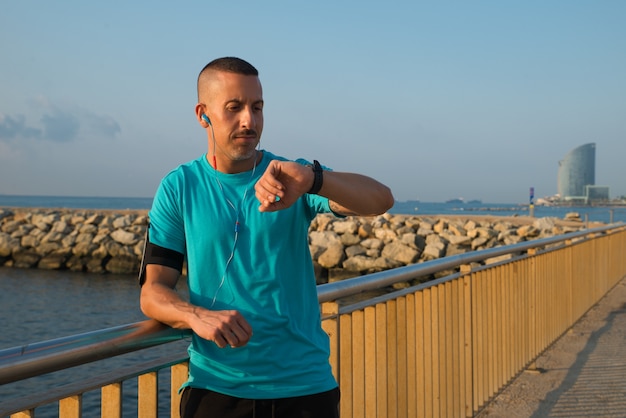 Serious male jogger looking at watch on bridge