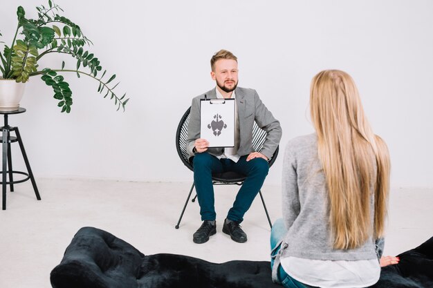 Serious male psychologist showing paper with rorschach inkblot to the female patient